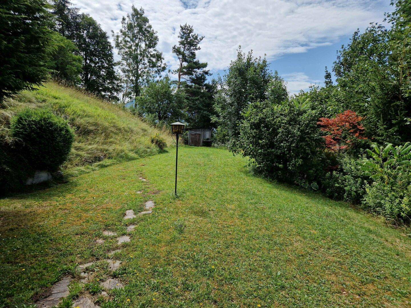 Großer, gepflegter Gartenbereich mit Rasenfläche und Bäumen, der sich an einem sanften Hang erstreckt.