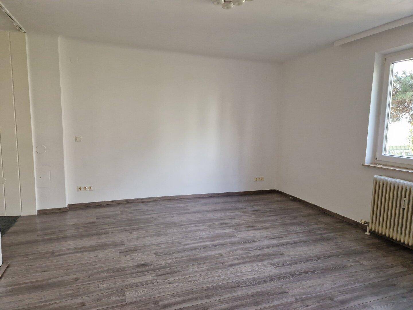 Leerer Wohnraum mit modernem Laminatboden und einem Fenster, das Tageslicht hereinlässt.