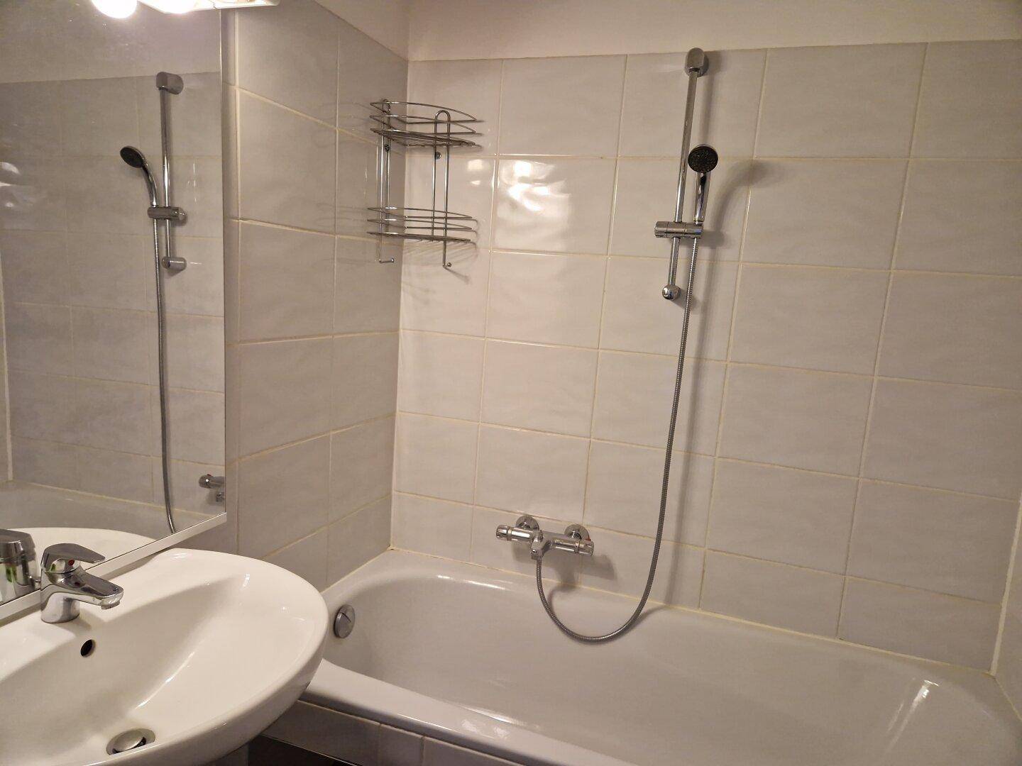 Helles Badezimmer mit weißen Fliesen, Badewanne mit Duschfunktion und einem Waschbecken.