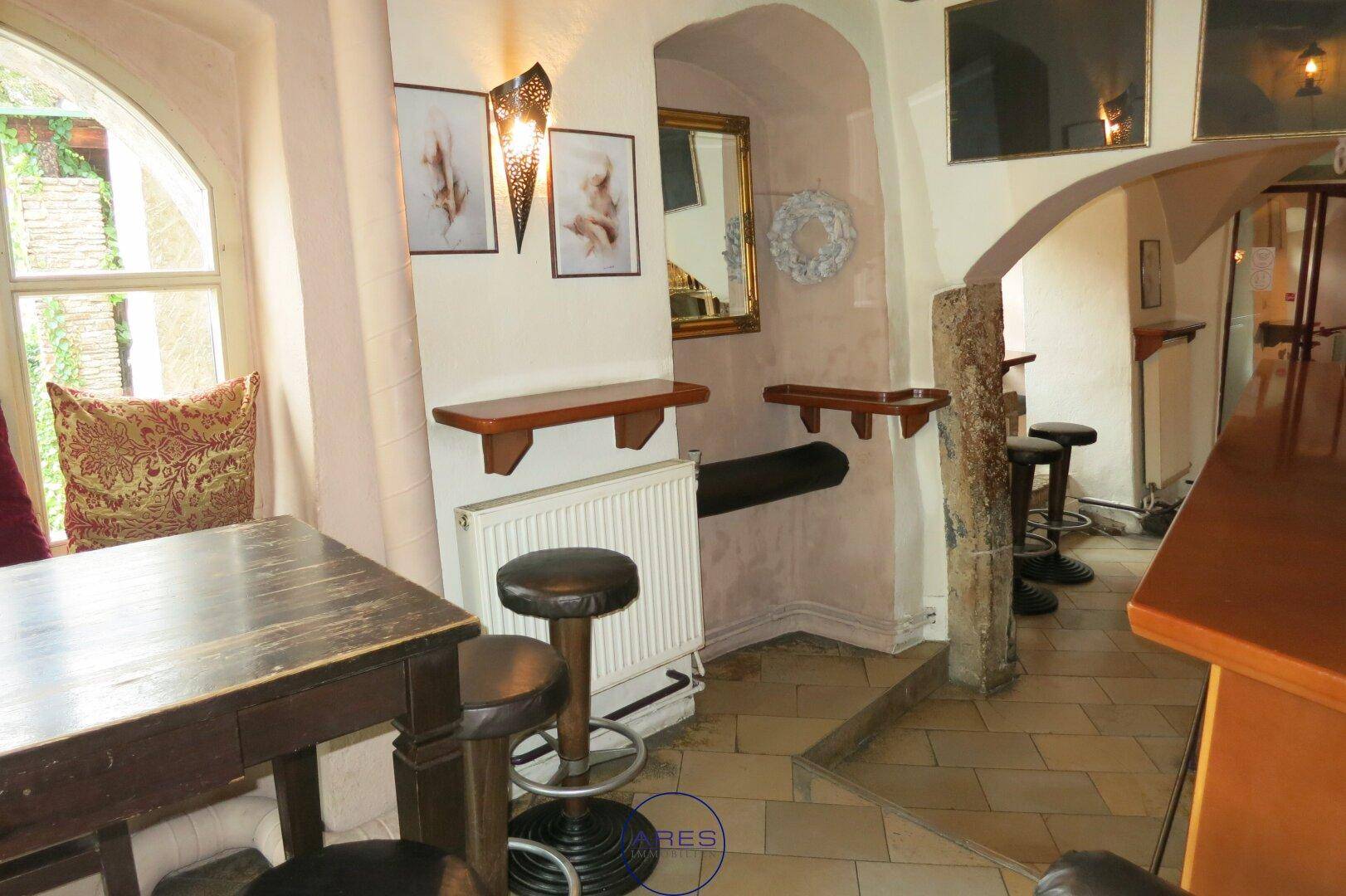 Gemütlicher Sitzbereich in einer Bar mit Holztischen, Barhockern und dekorativen Wandleuchten.