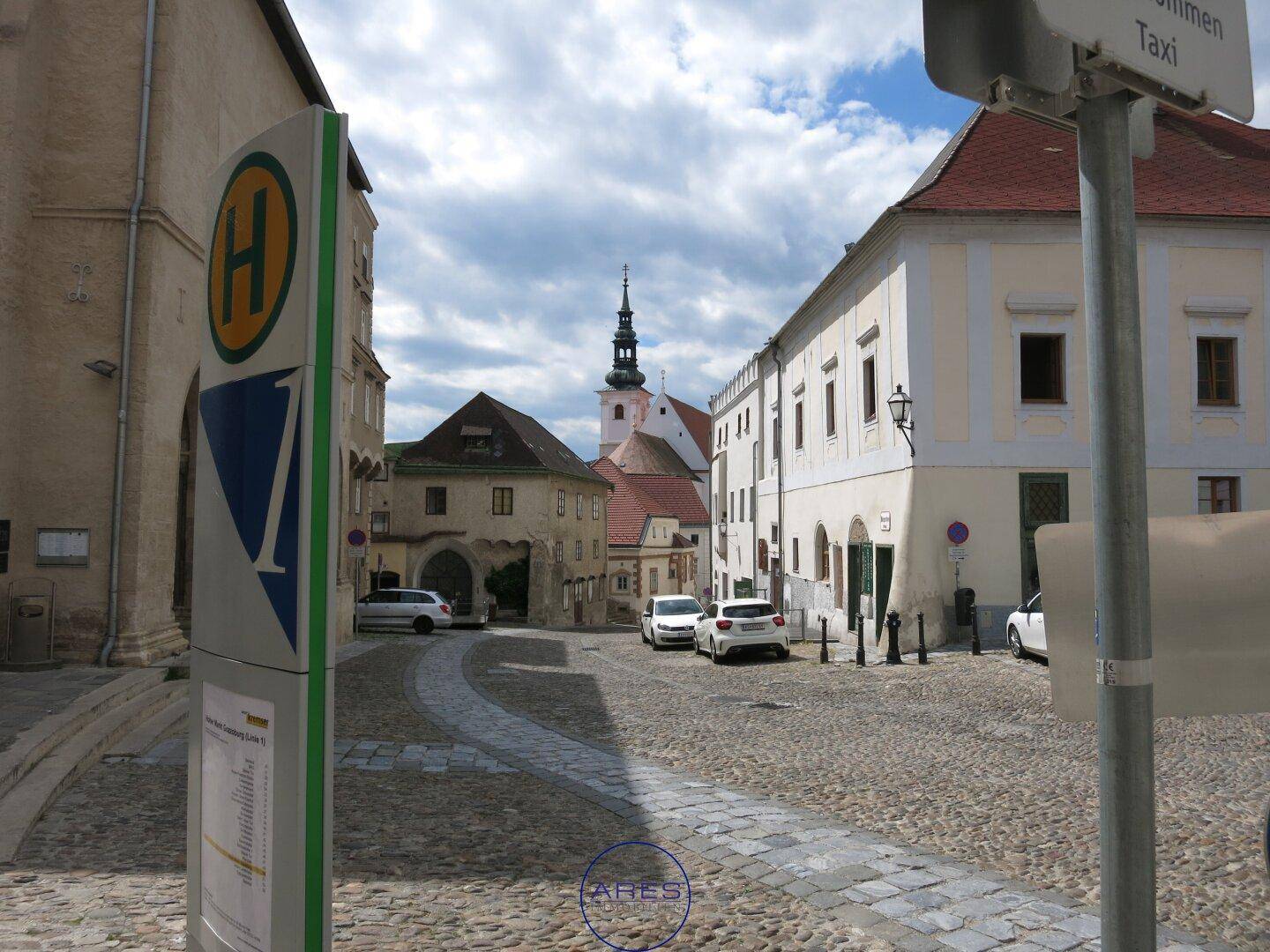 Historische Straße mit Kopfsteinpflaster, alten Gebäuden und einem Kirchturm im Hintergrund.