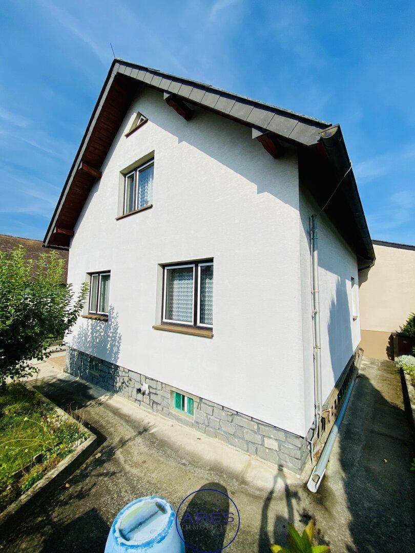 Seitenansicht des weißen Hauses mit kleinen Fenstern und Steinsockel.