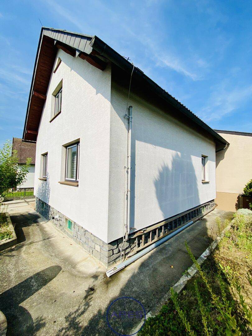 Seitenansicht des Hauses mit weißer Fassade und sichtbaren Regenrinnen.