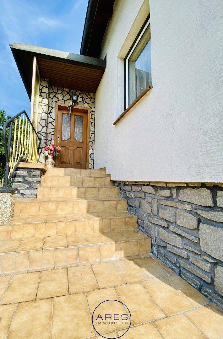 Detailansicht des Hauseingangs mit Steintreppe, Holztür und dekorativen Blumen.