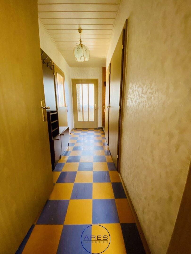Langer Flur mit gelb-blauen Fliesen und Holzdecke, der zu weiteren Räumen führt.