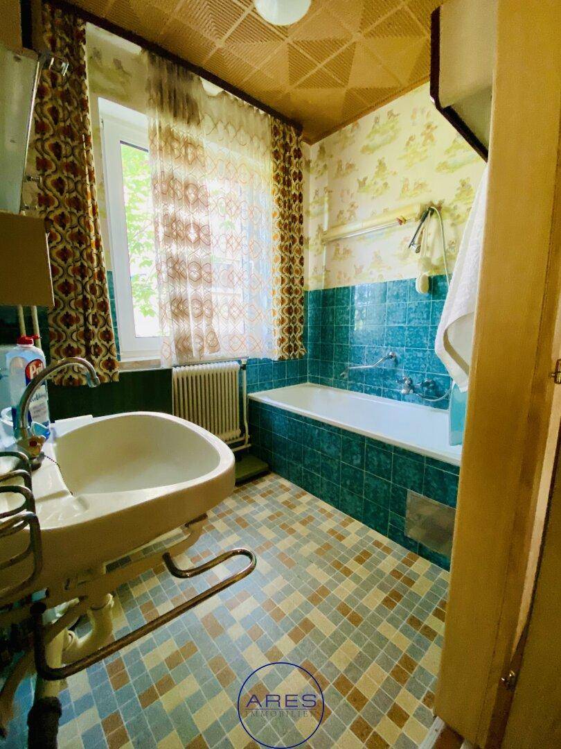 Badezimmer im 80er-Jahre-Stil mit blauen Fliesen, Badewanne und Fenster.