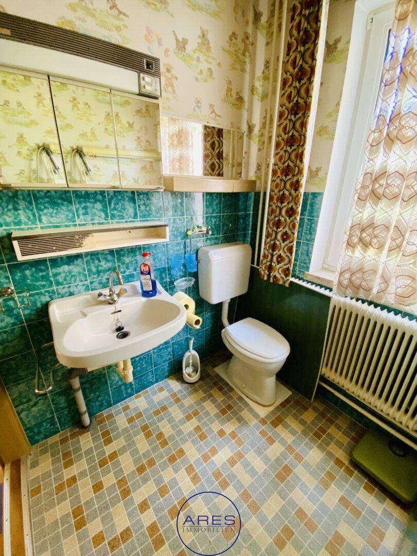 Badezimmer mit WC, Waschbecken und blauen Fliesen im Retro-Stil.