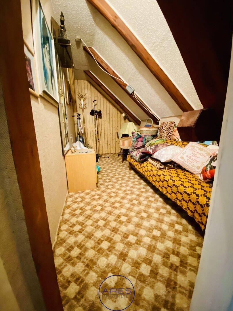 Dachzimmer mit Teppichboden, schrägen Wänden und sichtbaren Holzbalken.