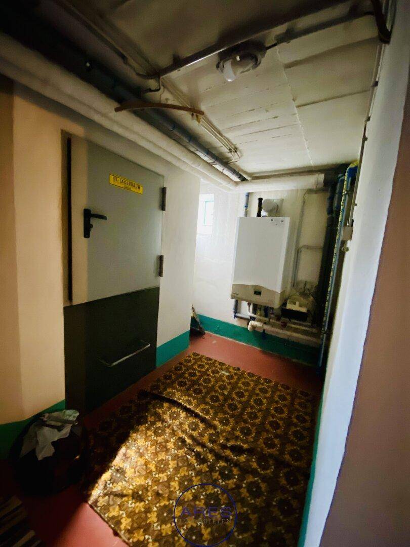 Kellerflur mit Wandheizkessel, sichtbaren Rohren und einem gemusterten Teppich auf dem Boden.