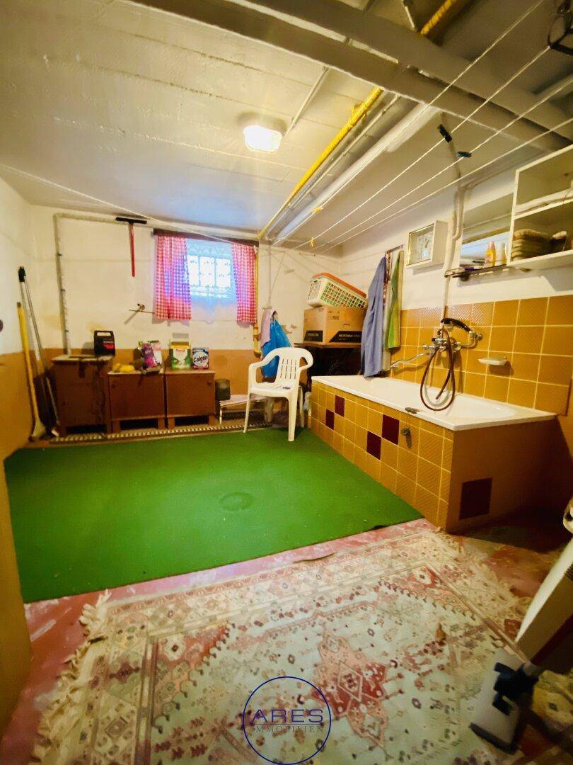 Mehrzweckraum im Keller mit Badewanne, gelben Fliesen und Wäscheleinen an der Decke.