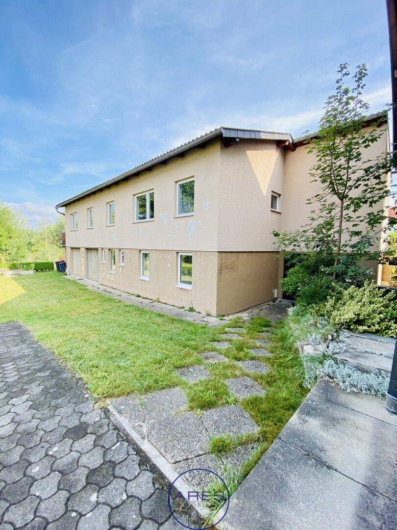 Seitenansicht des Gebäudes mit beigefarbener Fassade, Rasenfläche und gepflastertem Weg.