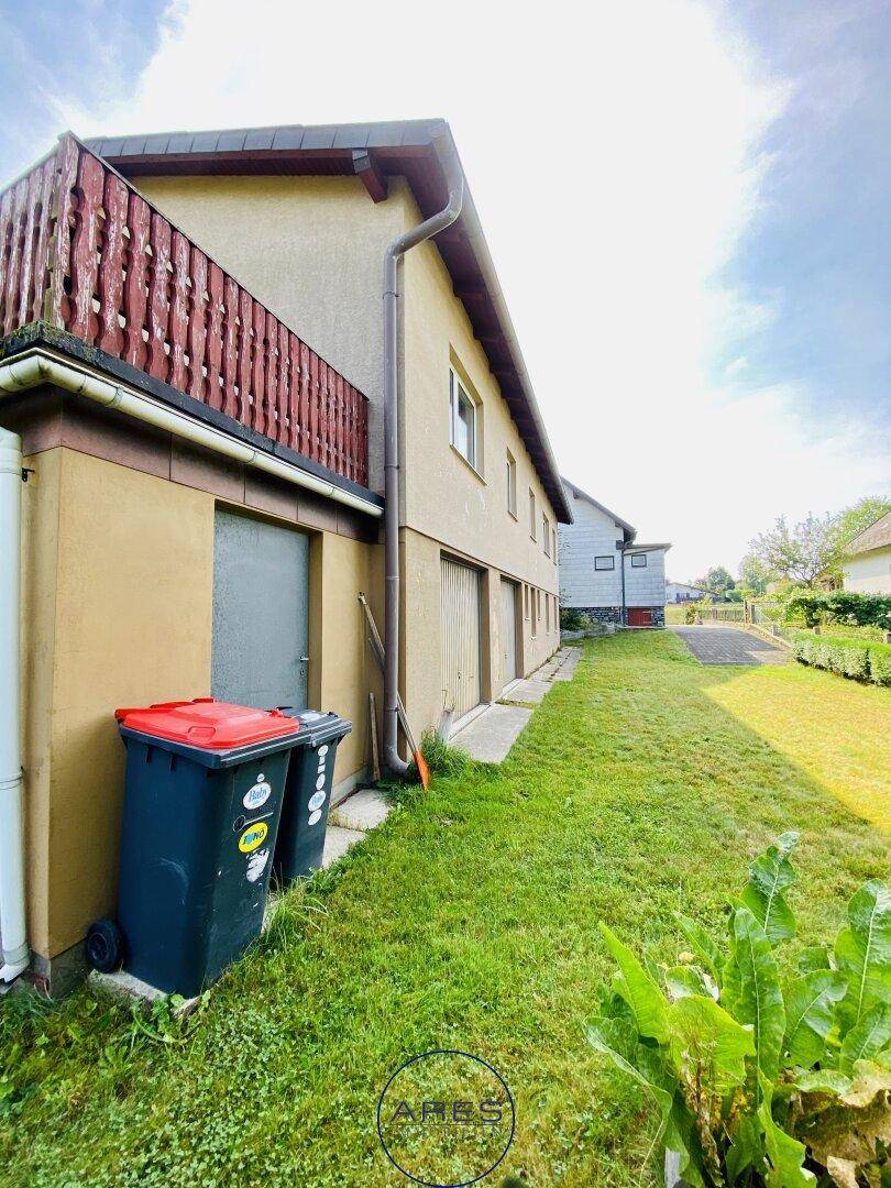 Seitenansicht des Hauses mit Balkon, Rasenfläche und Mülltonnen am Gebäude.