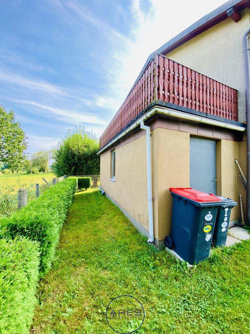 Seitenansicht des Hauses mit Balkon, gepflegter Hecke und weitläufiger Rasenfläche.