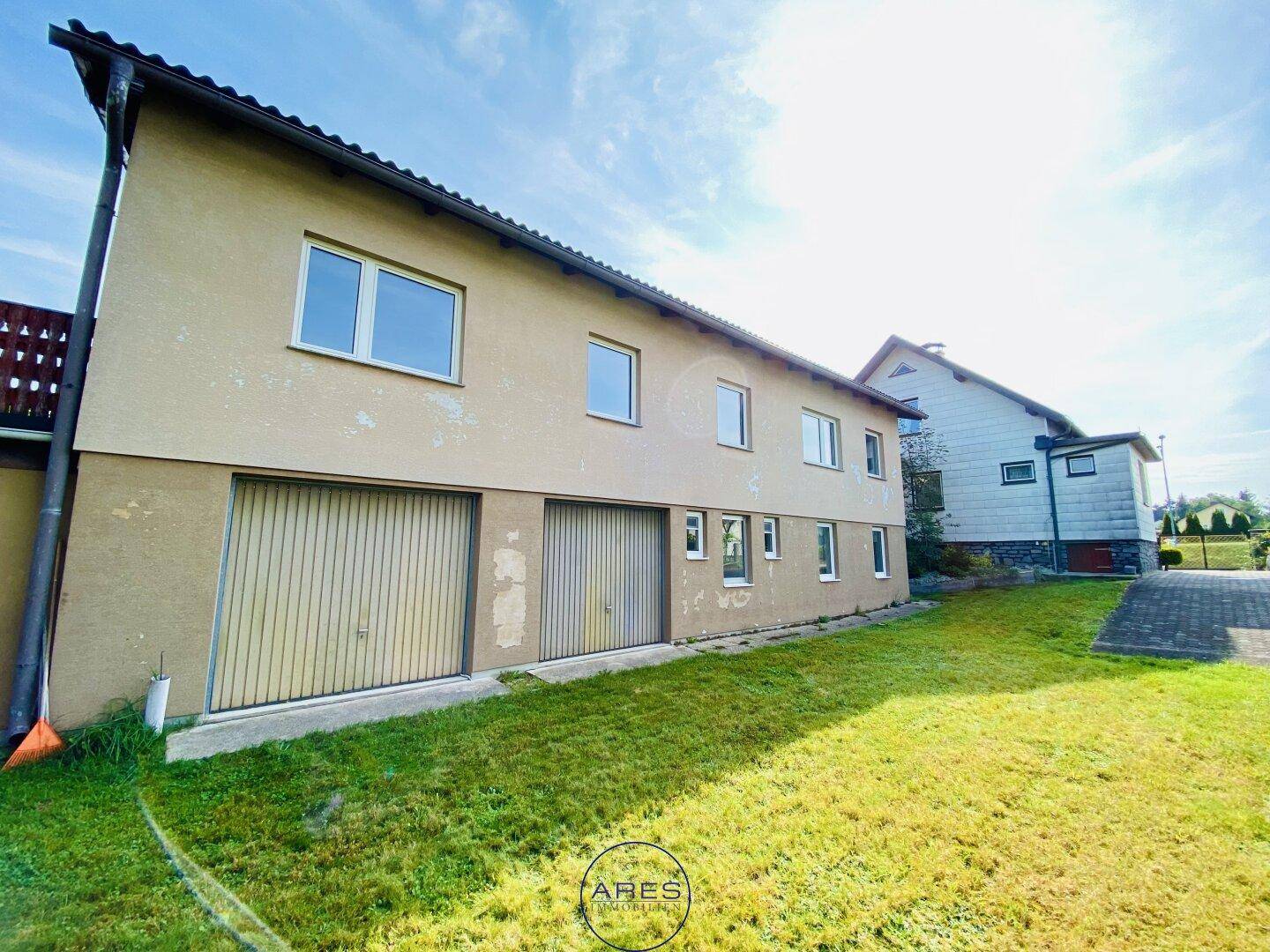 Rückseite des Hauses mit zwei Garagentoren und einer weitläufigen Rasenfläche.