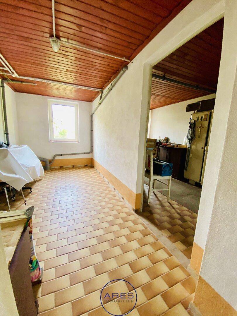 Flur mit gefliestem Boden und Holzdecke, der in einen angrenzenden Raum mit Kühlschrank führt.