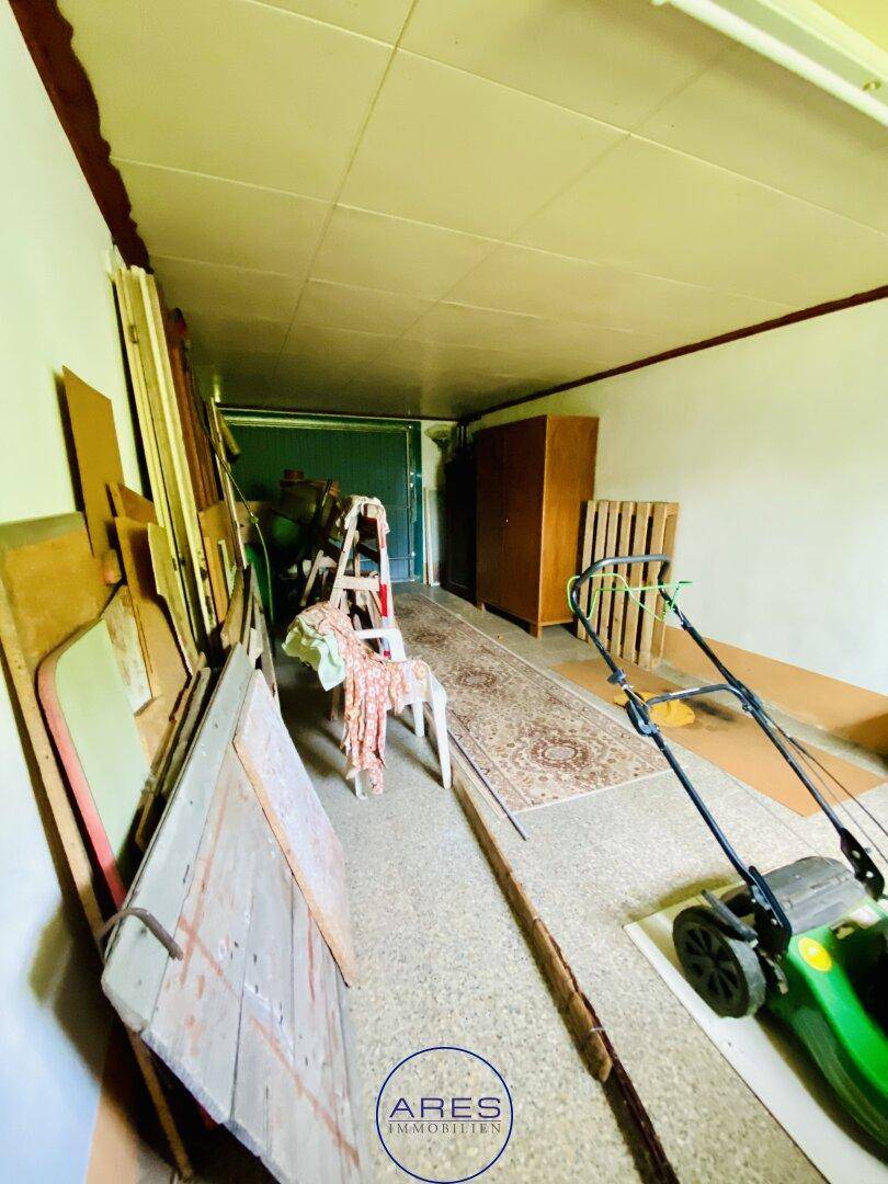 Garage mit Rasenmäher und weiteren Lagergegenständen, bietet viel Stauraum.