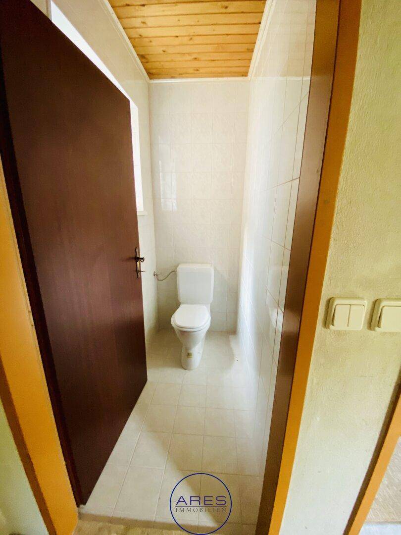 Kleines separates WC mit Toilette, gefliestem Boden und Holzdeckenverkleidung.