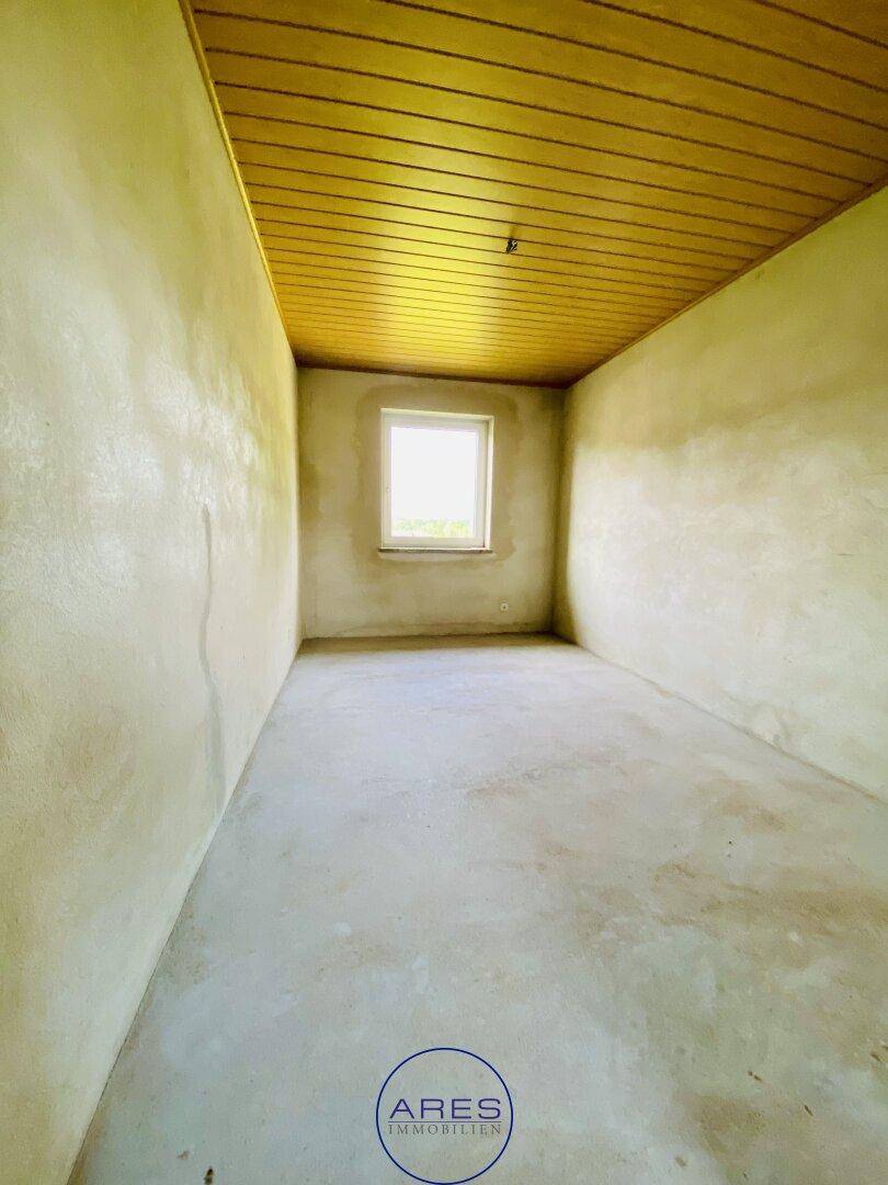 Leerer Raum mit hellen Wänden, Holzdeckenverkleidung und einem einzelnen Fenster.