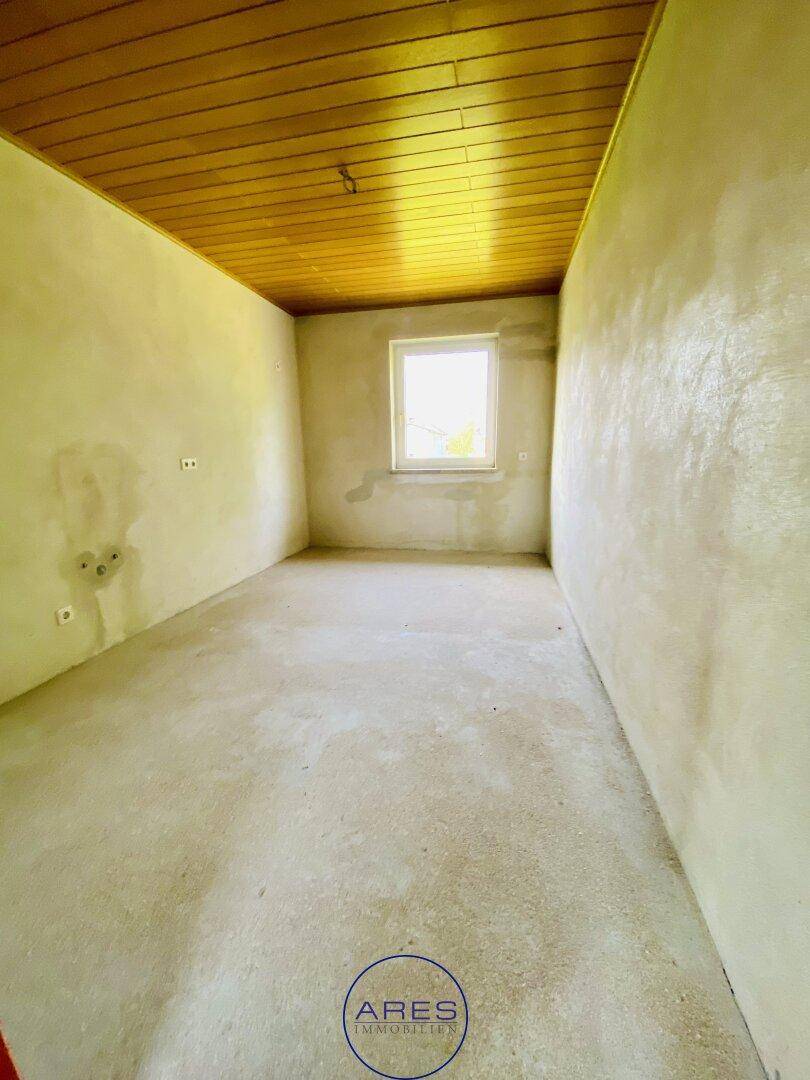 Leerer Raum mit Holzdecke und Fenster, bereit für den Ausbau und die individuelle Gestaltung.