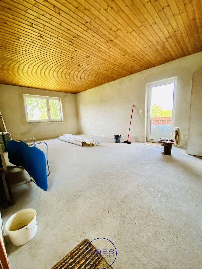 Geräumiger, unfertiger Raum mit Holzdecke und Zugang zum Außenbereich, ideal für Renovierungsprojekte.
