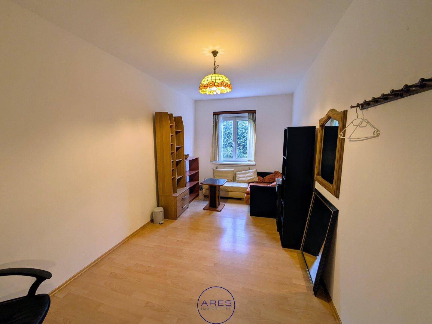Vielseitiger Raum mit Holzboden, Fenster und Regalen, ideal als Büro oder Gästezimmer.