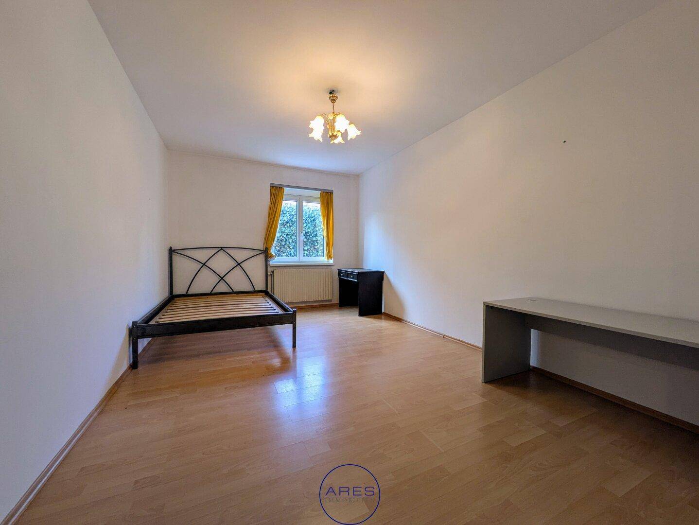 Schlafzimmer mit Holzboden, Fenster und einfacher Einrichtung, bereit zur individuellen Gestaltung.