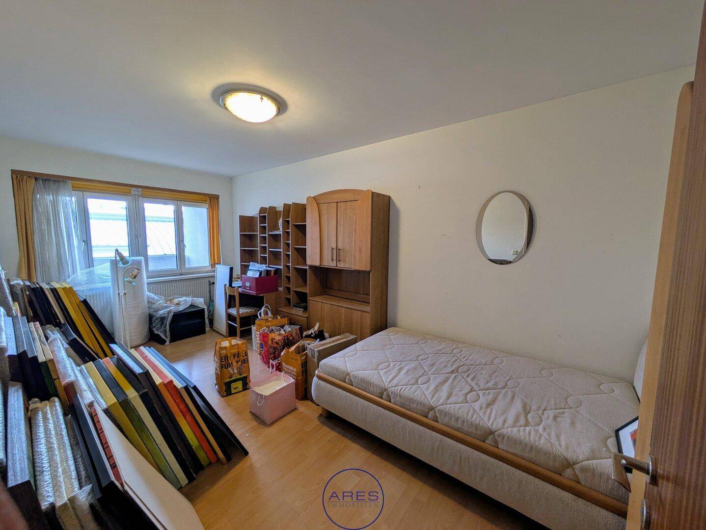 Schlafzimmer mit Holzboden und Fenster, derzeit als Stauraum genutzt, bietet viel Potenzial.