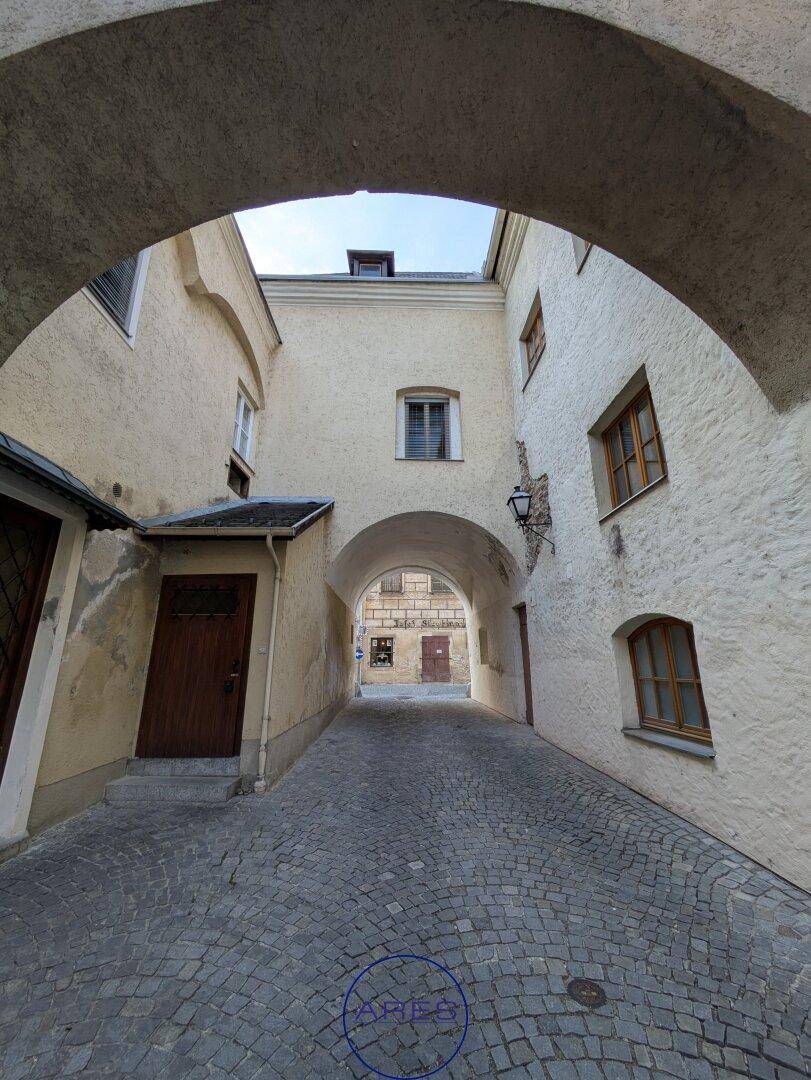 Historischer Durchgang mit Kopfsteinpflaster und weiteren Bögen, der zu einem Innenhof führt.