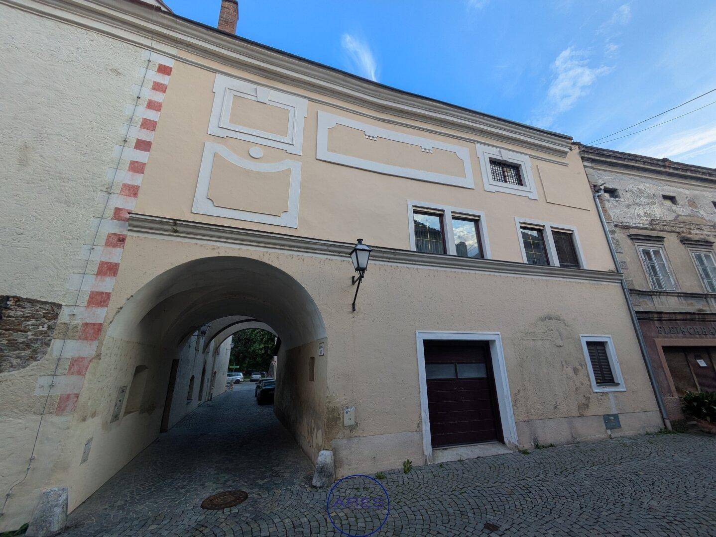 Historische Fassade mit dekorativen Elementen und einem Torbogen, der zu einem Durchgang führt.