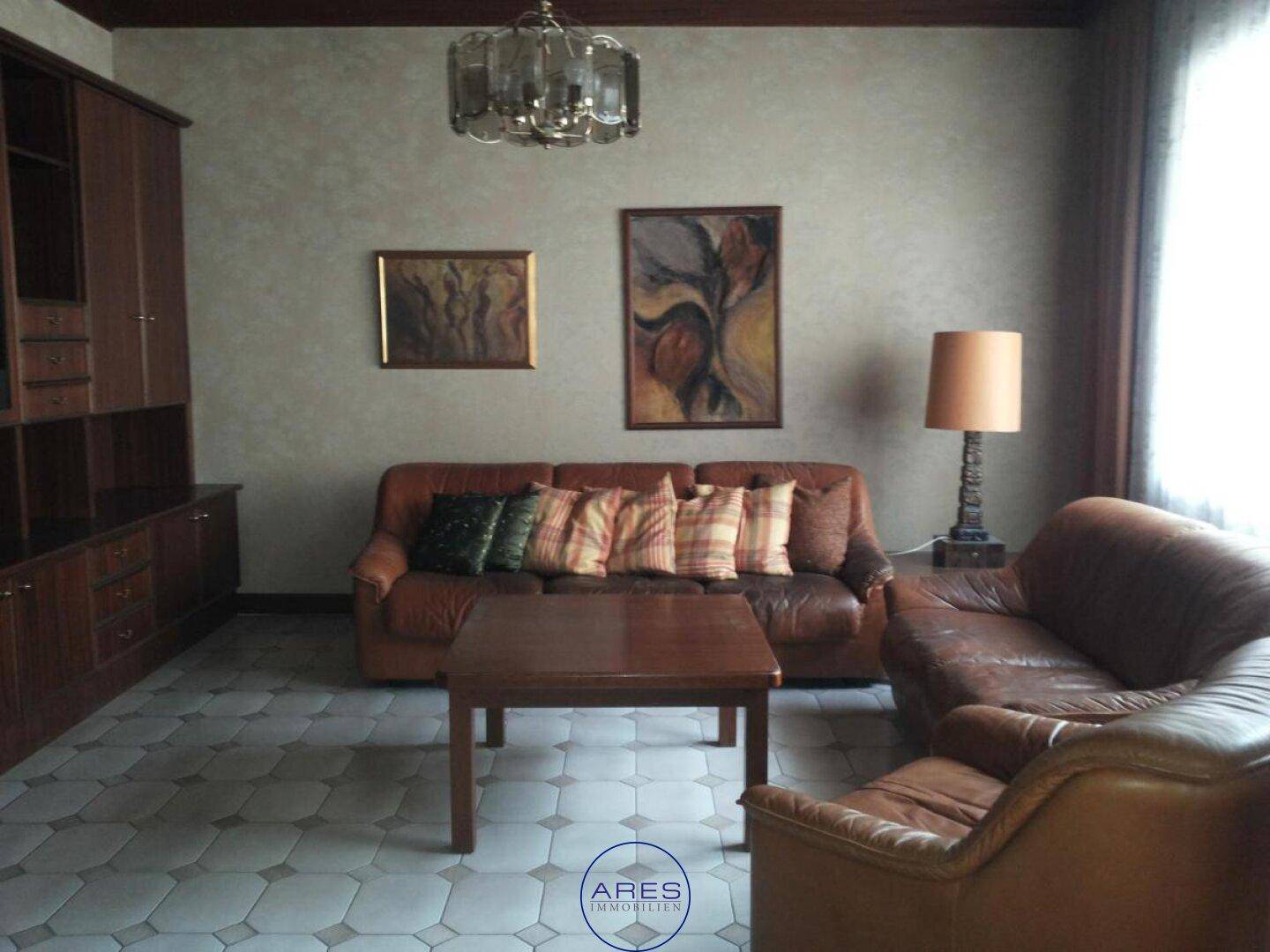 Gemütliches Wohnzimmer mit Ledersofas, Holzmöbeln und gemusterten Fliesenböden.
