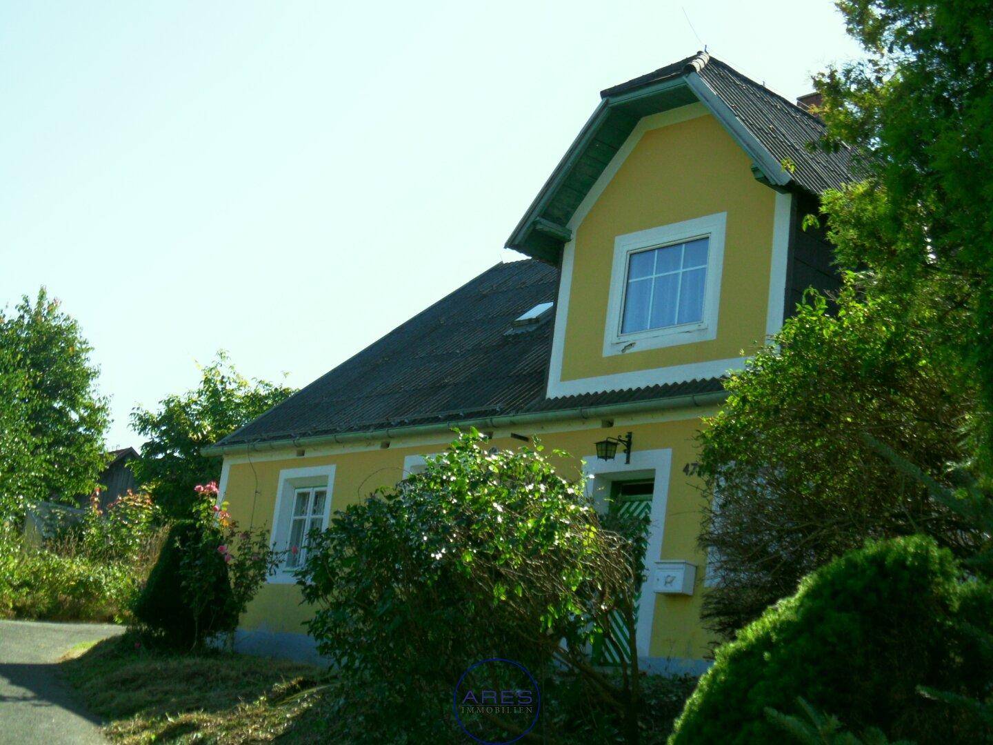 Detailansicht der gelben Hausfassade mit weißen Fenstern und grüner Eingangstür unter klarem Himmel.