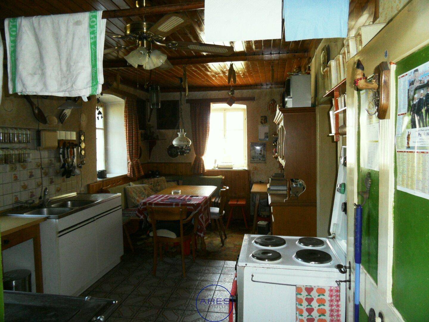 Rustikale Küche mit Holzbalkendecke, Kachelofen und Essbereich, ausgestattet mit traditionellen Geräten.