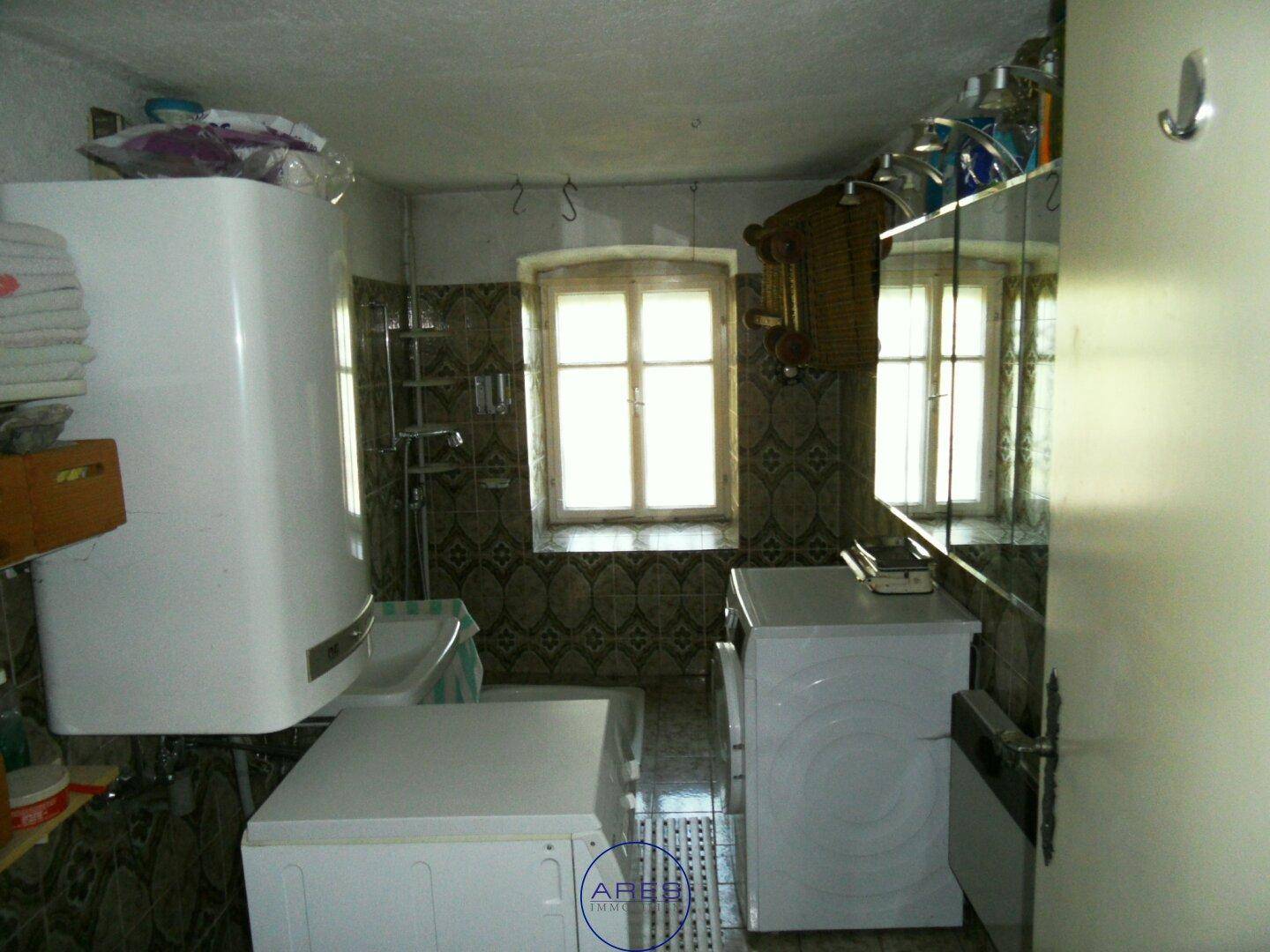 Badezimmer mit Waschmaschine, Boiler und gemusterten Fliesen, ausgestattet mit einem Fenster.