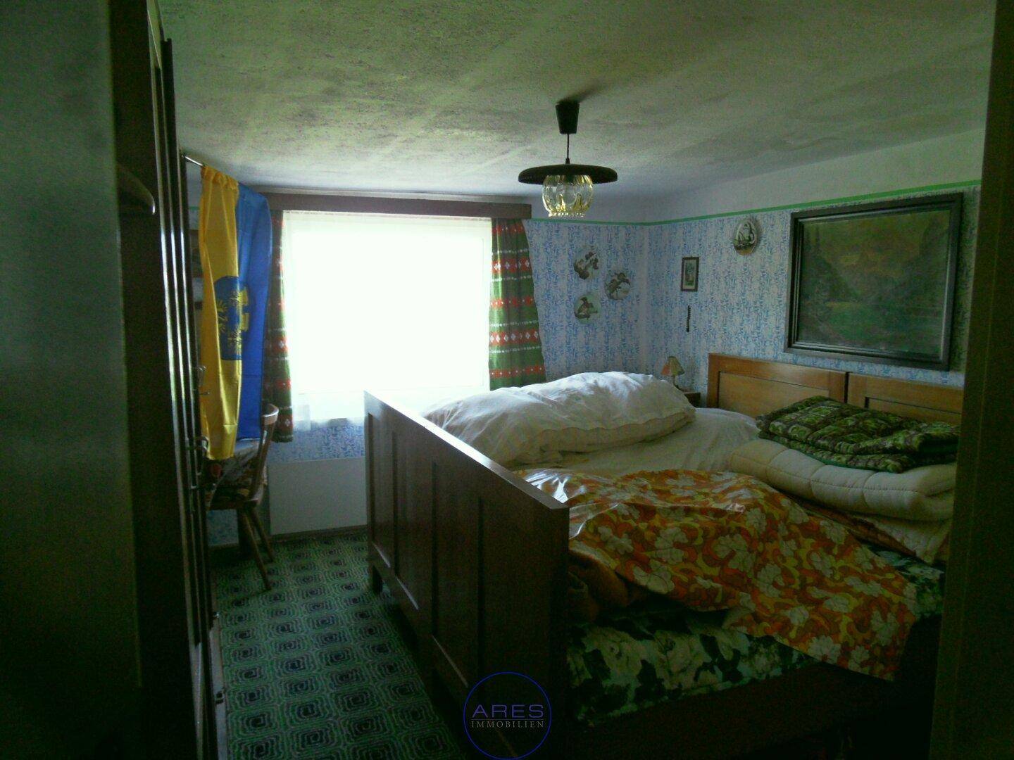 Schlafzimmer im Dachgeschoss mit schrägen Wänden, Teppichboden und einem großen Fenster.