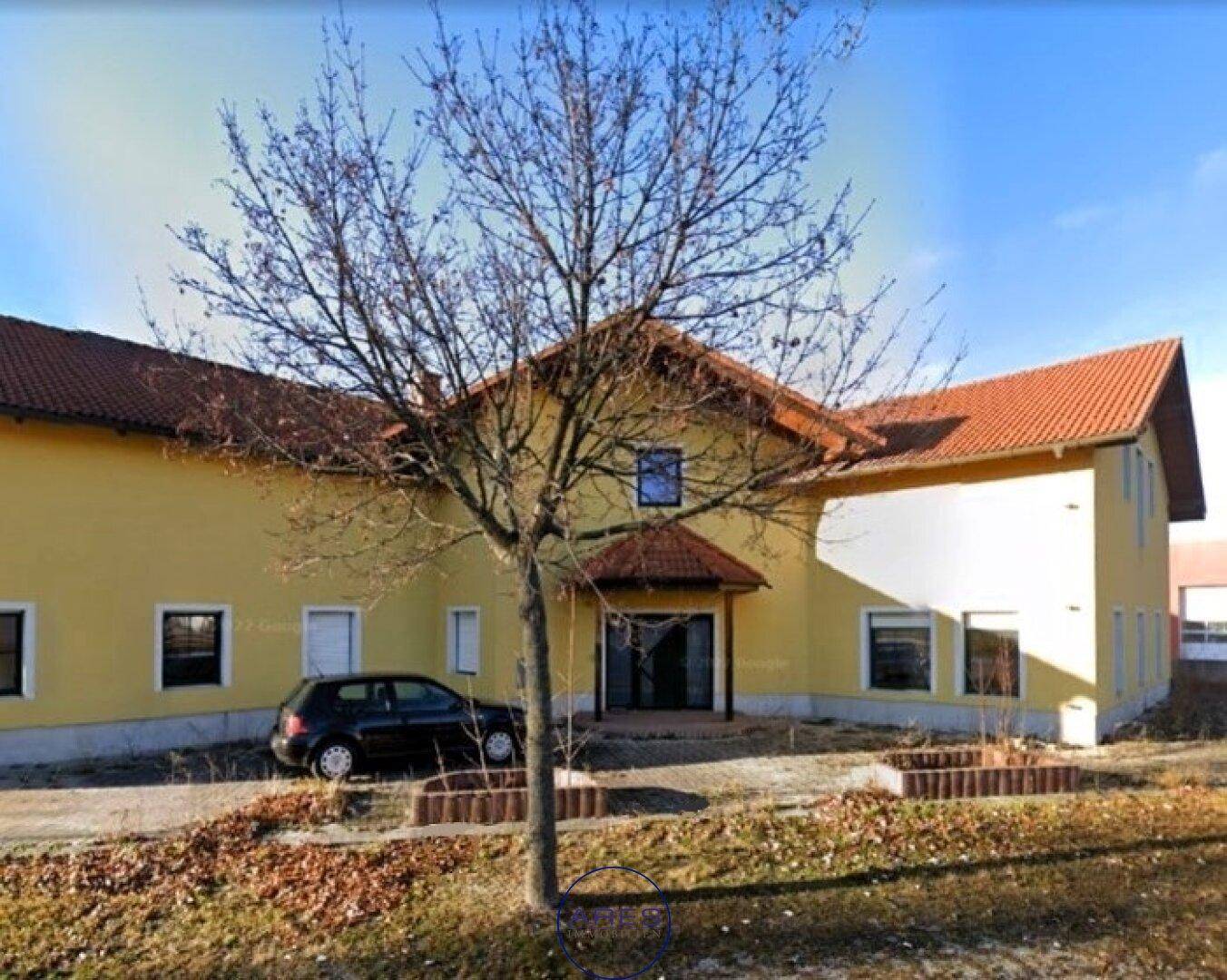 Gelbes Gebäude mit rotem Ziegeldach und kahlen Bäumen an einer Straße im Winter.
