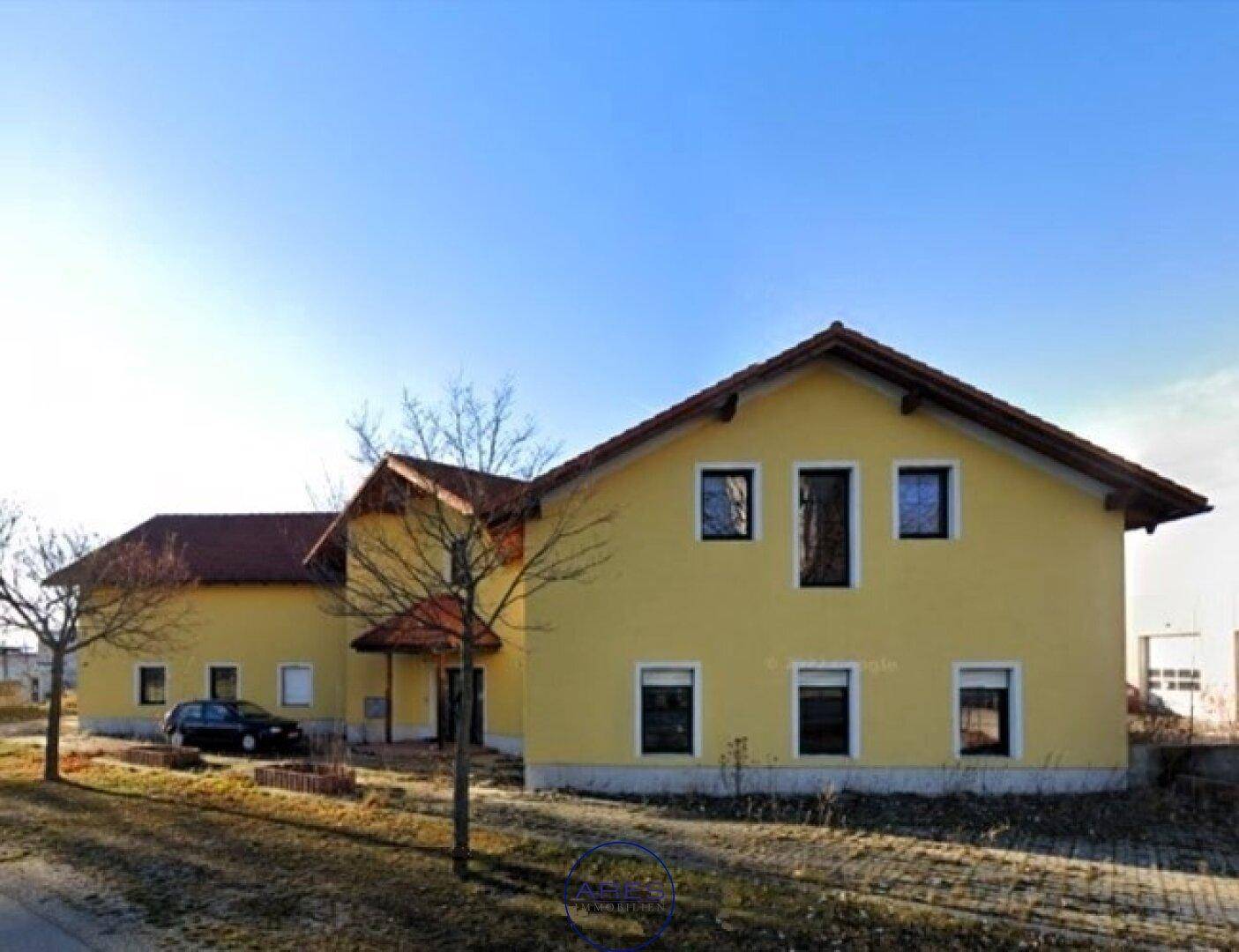 Gelbes Gebäude mit rotem Ziegeldach und kahlen Bäumen an einer Straße im Winter.