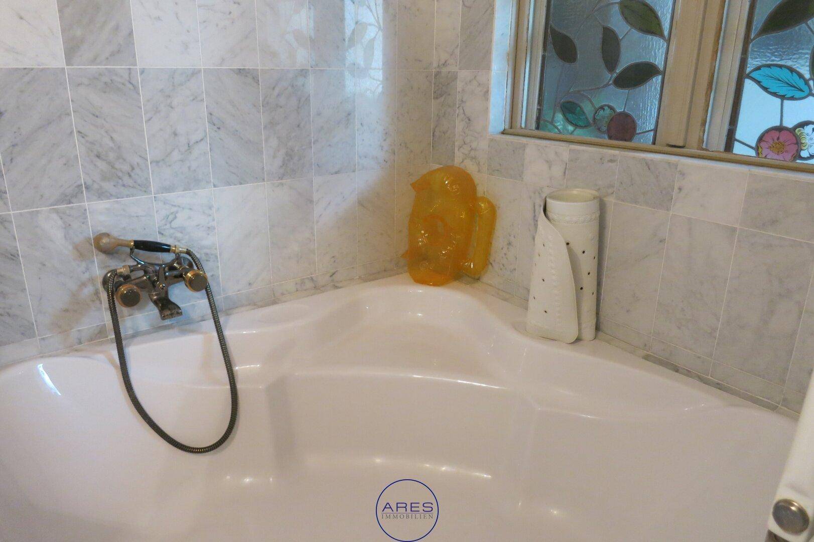 Badezimmer mit Eckbadewanne und Marmorfliesen, ergänzt durch ein farbiges Bleiglasfenster.