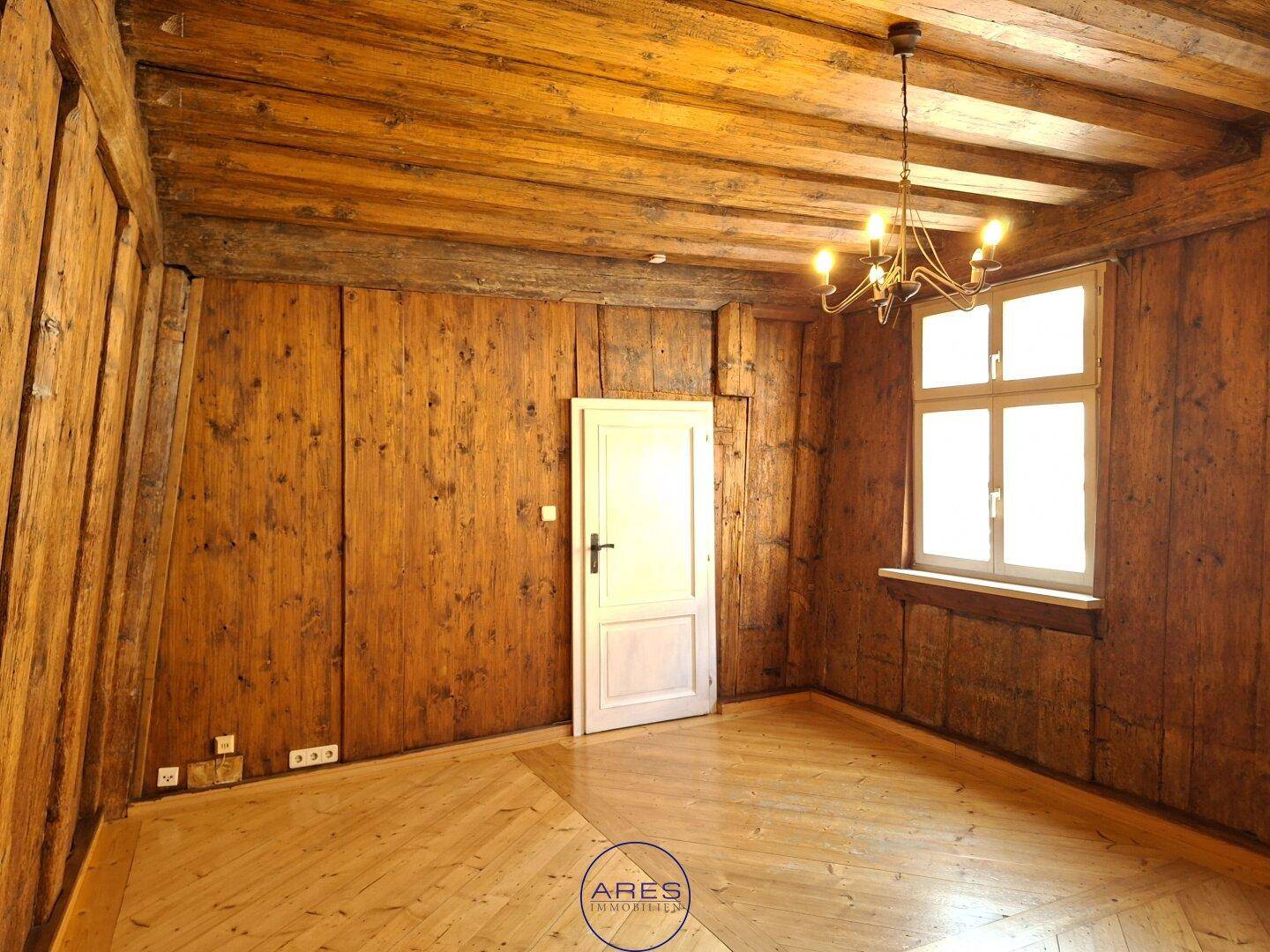 Raum mit vollständiger Holzvertäfelung an Wänden und Decke sowie hellem Parkettboden.