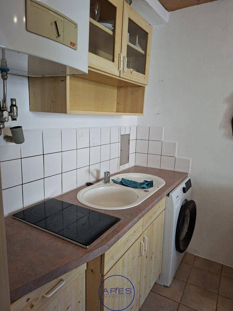 Funktionale Küche mit Holzschränken, Spüle, Kochfeld und Waschmaschine unter der Arbeitsplatte.