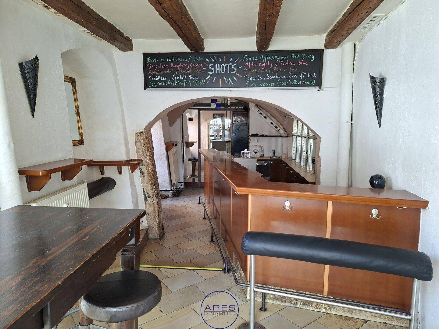 Bar-Bereich mit Holzbalken, Theke und Regalen, der eine rustikale Atmosphäre schafft.