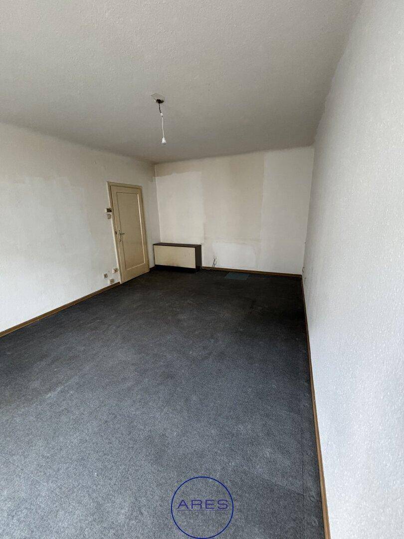 Geräumiges Zimmer mit Teppichboden, weiß gestrichenen Wänden und einer einfachen Tür.