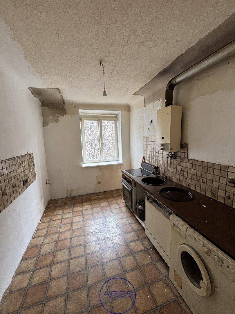 Renovierungsbedürftige Küche mit alten Fliesen, Spüle und einem Fenster.