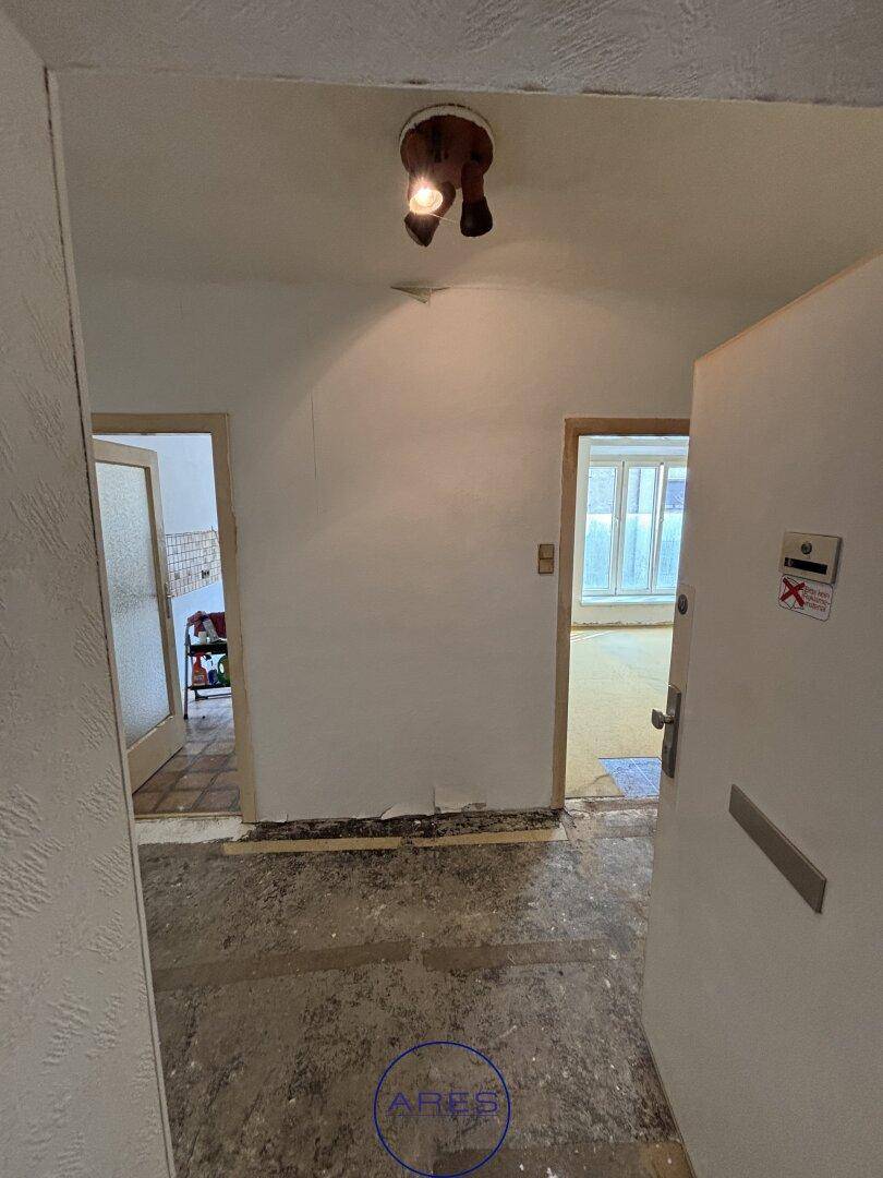 Eingangsbereich mit freigelegtem Unterboden, weiß gestrichenen Wänden und mehreren Türen.