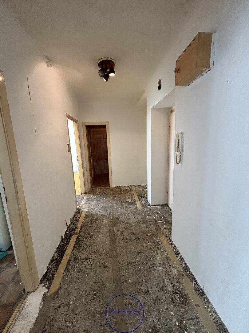 Flur mit sichtbarem Unterboden, weiß gestrichenen Wänden und einer Gegensprechanlage.