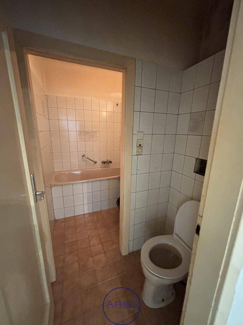 Separates WC mit Fliesenboden und Blick in ein angrenzendes Badezimmer mit Badewanne.