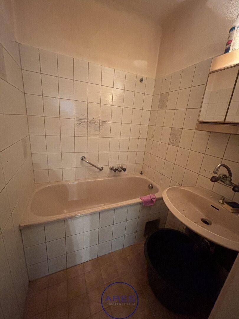 Badezimmer mit Badewanne, Waschbecken und weißen Wandfliesen im Originalzustand.