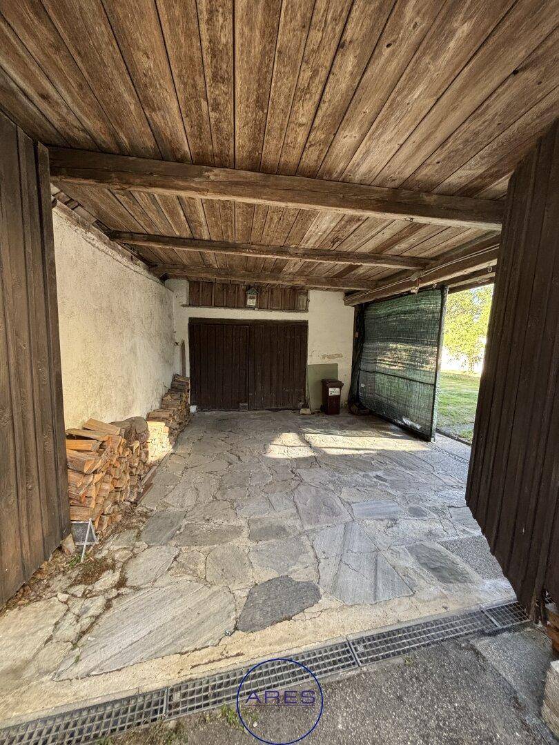Überdachter Außenbereich mit Steinboden, Holzdecke und gestapeltem Brennholz.