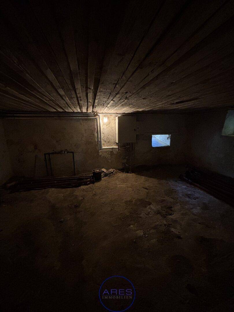 Dunkler Kellerraum mit Holzbalkendecke und kleinem Fenster, ideal zur Lagerung.