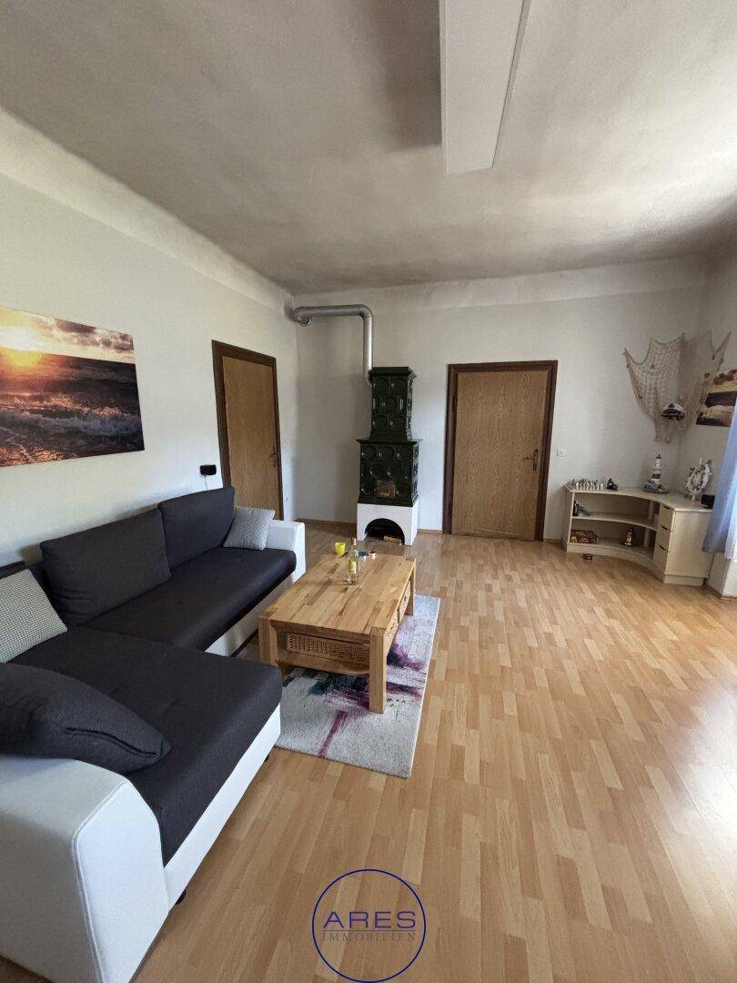 Gemütliches Wohnzimmer mit Ecksofa, Holzboden und traditionellem Kachelofen.