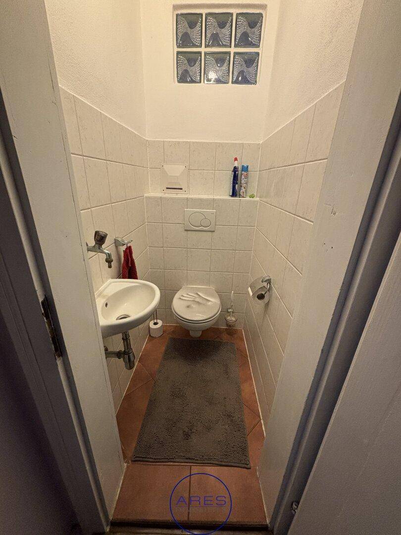 Kleines Gäste-WC mit Toilette, Waschbecken und Fliesen an Wänden und Boden.